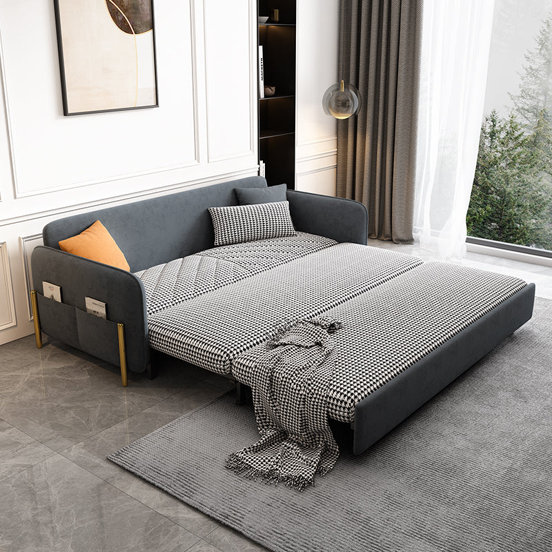 Gray velvet sleeper sofa with pull-out drawer in a guest room with curtains and a rug.
